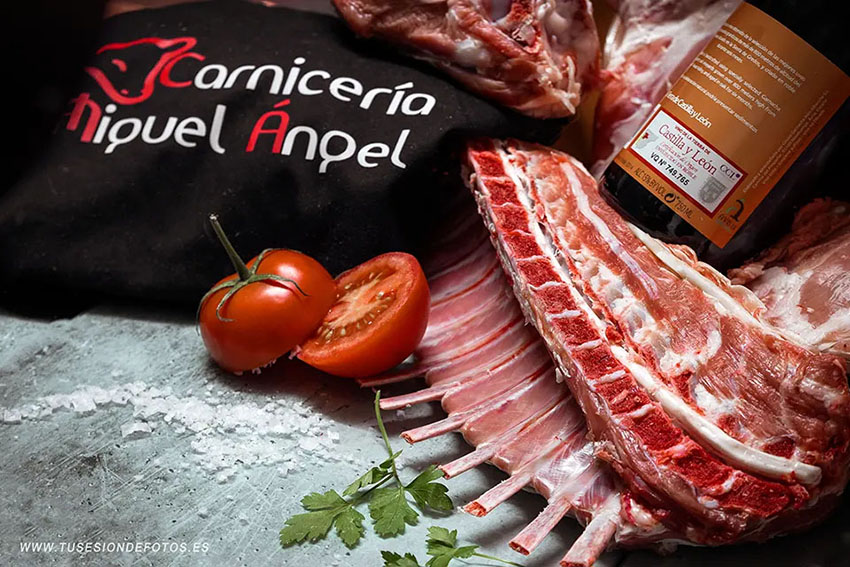 fotografía de un bodegon con despieces de cabrito y  cordero, una botella de vino y un tomate